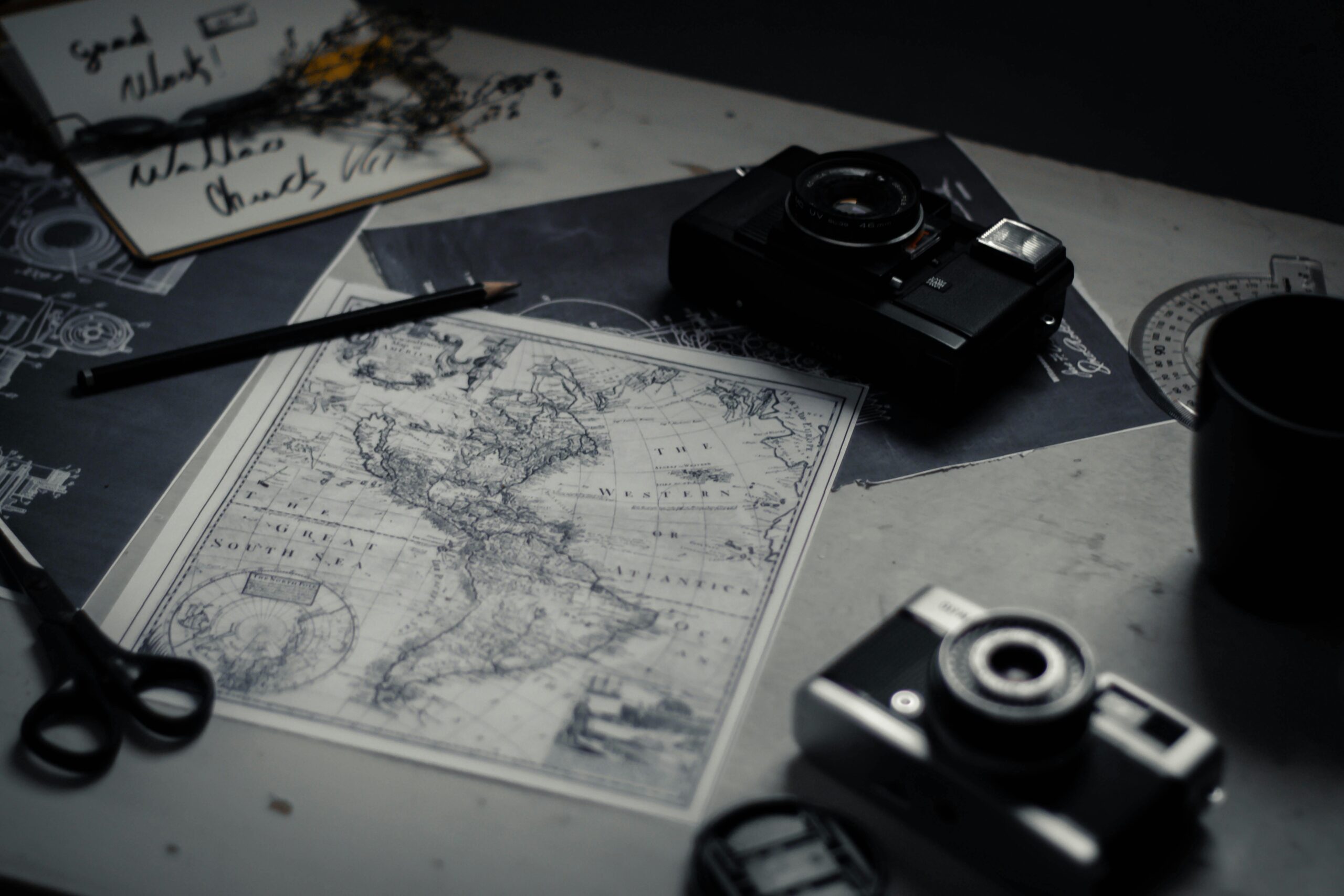 Electronic devices for taking photo and scissors with pencil composing with herbarium and detailed map of world on table in room